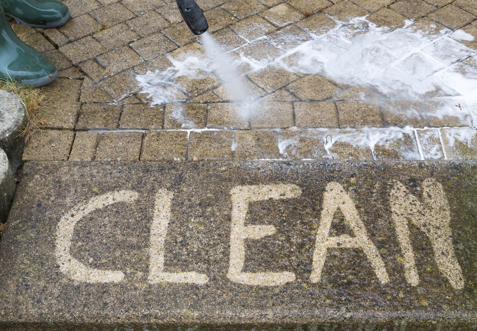 Pressure washing revealing the word CLEAN on pavers